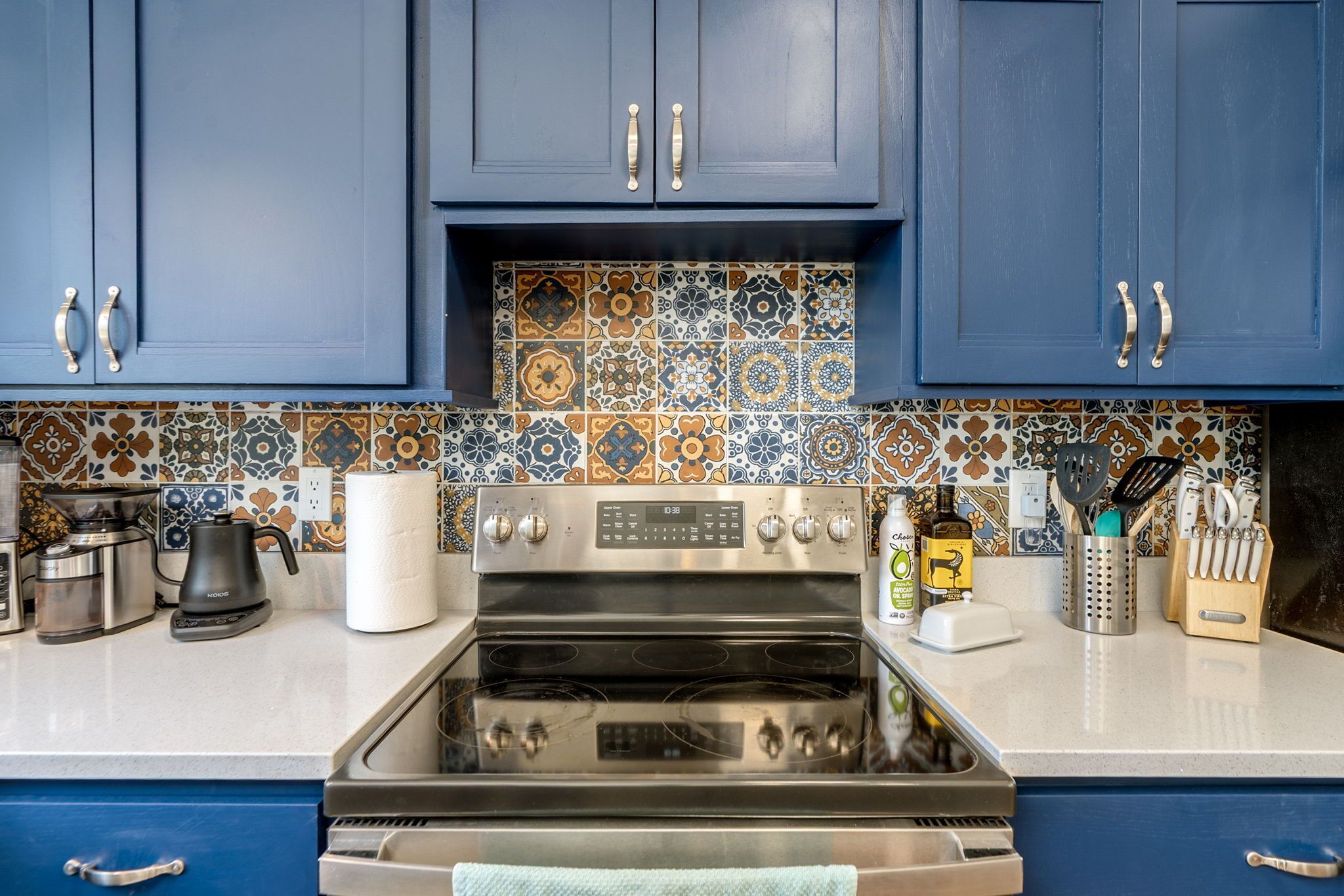 Een keuken met blauwe kastjes, een roestvrijstalen fornuis en een kleurrijke tegelachtergrond.