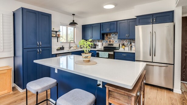A modern kitchen with blue cabinets, a stainless steel refrigerator, and a central island with stools. - Oasis Escape: Quiet & Convenient (Tucson)