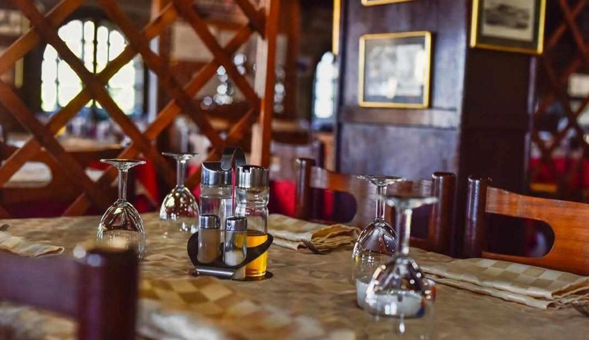 L’intérieur d’un restaurant avec une nappe à carreaux, plusieurs verres à vin et un pichet en métal sur la table.