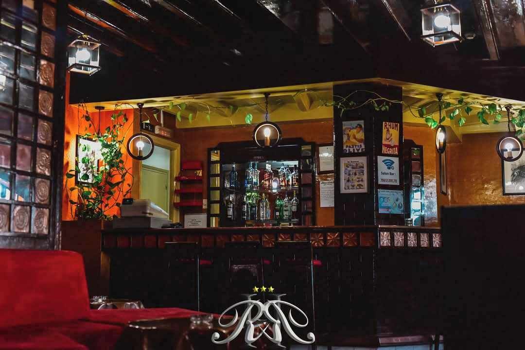 Una zona de bar con mostrador, plantas colgantes y un letrero de neón.