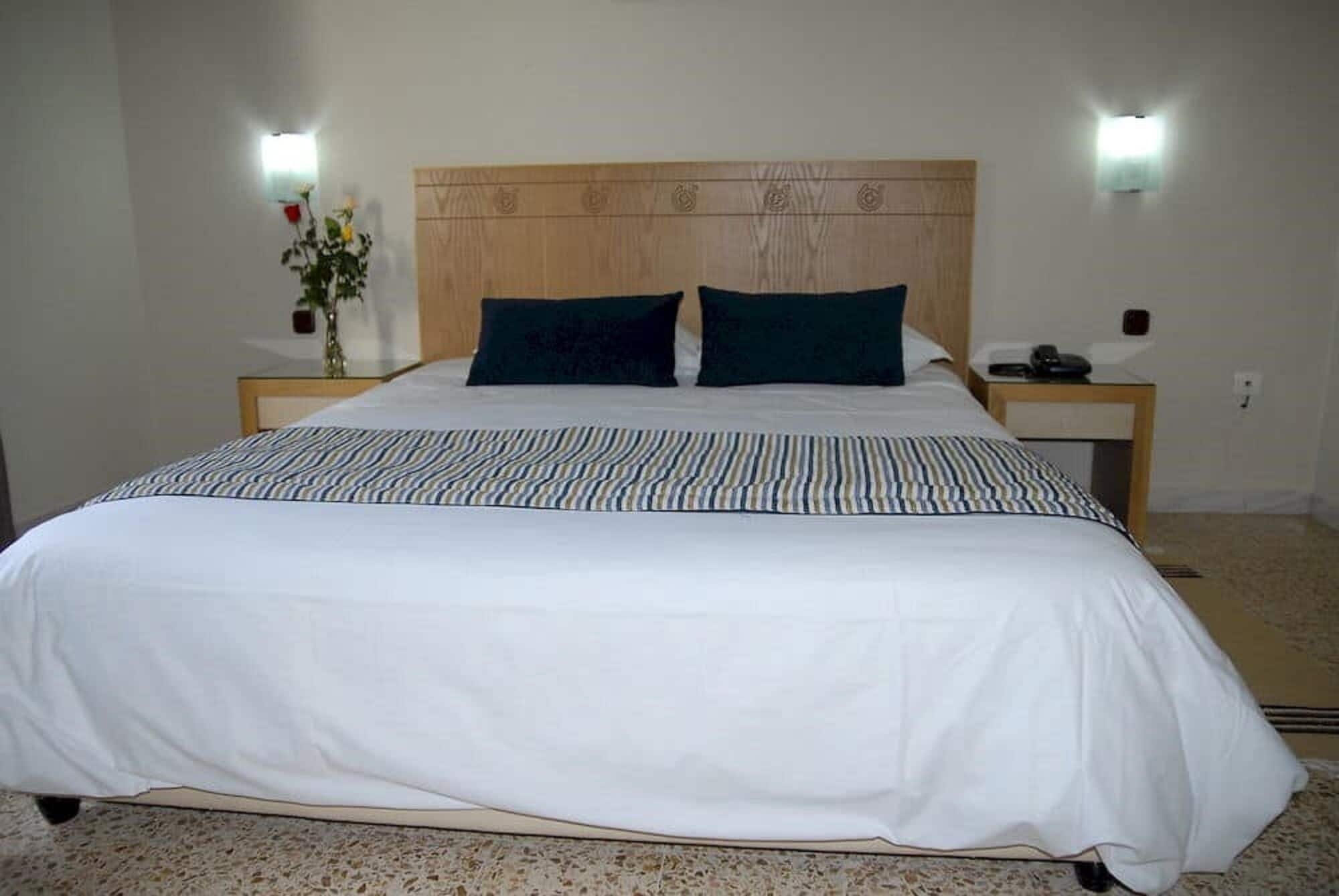A large bed with a wooden headboard, two bedside tables, and a decorative vase on one table.