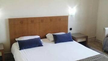Habitación de hotel con una cama grande, cabecera de madera, un cuadro en la pared y un equipo de aire acondicionado.