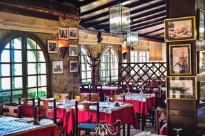 A restaurant with multiple tables covered in red tablecloths, wooden chairs, and a rustic interior with exposed beams and arched windows. - Rihana Hotel - Ain Draham (Ain Draham)