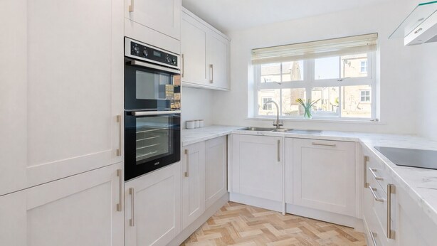 A modern kitchen with white cabinetry, a double oven, a sink, and a window with blinds. - Modern 4-bed home near Thirsk| Ideal for Groups, Families & Work Stays (Rainton)