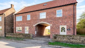 A two-story brick building with a red-tiled roof, a stone wall, and a small archway entrance. - Modern 4-bed home near Thirsk| Ideal for Groups, Families & Work Stays (Rainton)