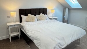 A bedroom with a sloped ceiling, a skylight, a bed with white bedding, two bedside tables with lamps, and a small nightstand. - Modern 4-bed home near Thirsk| Ideal for Groups, Families & Work Stays (Rainton)