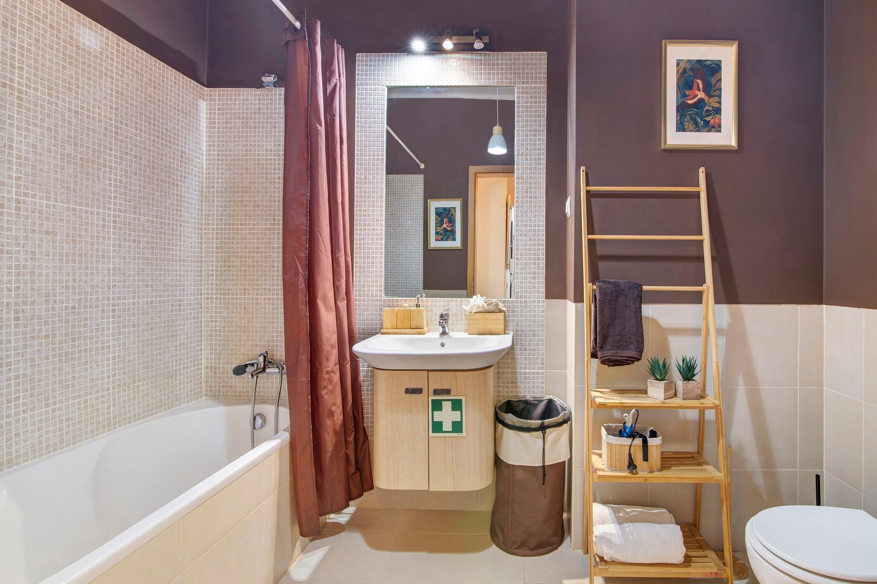 A bathroom with a bathtub, sink, mirror, shower curtain, and a shelf with toiletries.