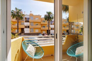 Un balcón con dos sillas y vista a un edificio amarillo, además de coches estacionados.