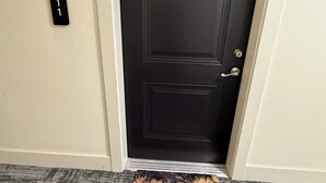 Una puerta negra con un pequeño emblema decorativo encima, un timbre y un felpudo de mármol blanco y negro en el frente.