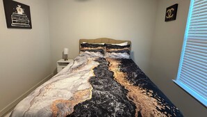 Un dormitorio con cama, mesita de noche, ventilador de techo y dos cuadros.