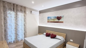 A modern bedroom with a wooden bed, a nightstand, a desk, and a wall-mounted air conditioner. - APARTMENT FREE SHUTTLE (Catania)