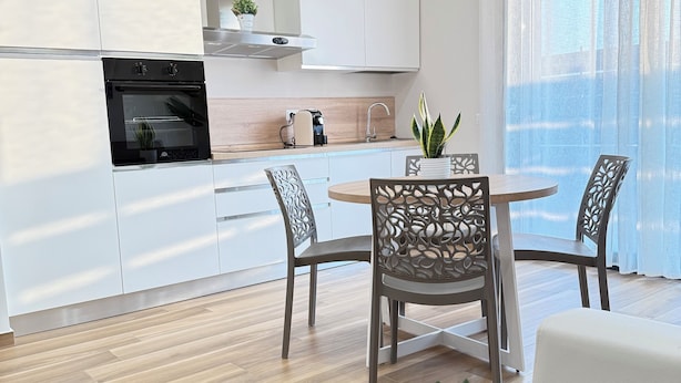 A modern kitchen with white cabinets, a built-in oven, and a dining area with a round table and chairs. - APARTMENT FREE SHUTTLE (Catania)