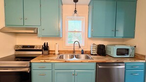 Una cocina con gabinetes color turquesa, un lavaplatos de acero inoxidable, un microondas, una estufa y un lavavajillas.