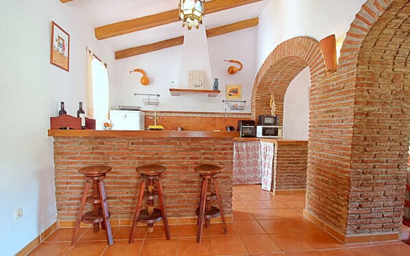 A kitchen with a brick wall, wooden stools, a white refrigerator, and a microwave.