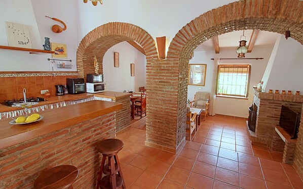 A kitchen with brick arches, a dining area with a table and chairs, and a fireplace.