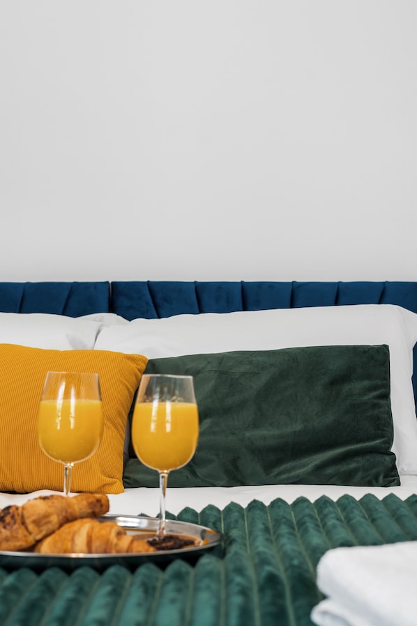 A neatly made bed with a blue headboard, white and green pillows, and a tray with croissants and orange juice glasses.