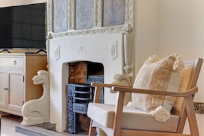 Una habitación con chimenea, televisor, armario y una silla con cojín.