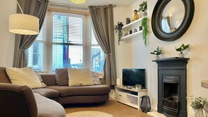 A living room with a sofa, TV, fireplace, and a large window with curtains. - Beautiful 2-bed Apartment In The Heart Of The City (Brighton and Hove)