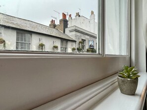 A window with a potted plant on a ledge, overlooking a building with a sign reading 'LORD NELSON'.