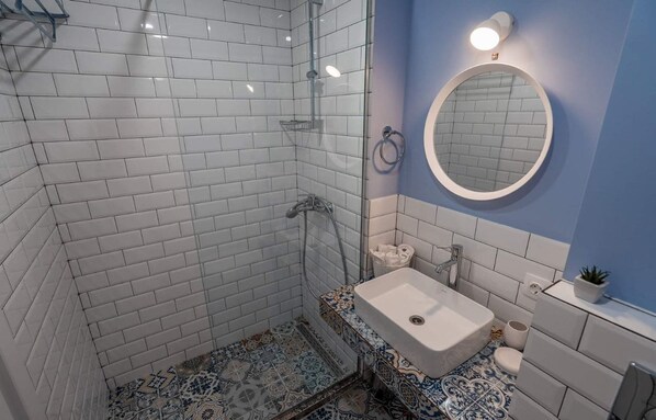 A bathroom with white subway tiles, a shower with a glass door, a sink with a decorative tile backsplash, and a round mirror on the wall.
