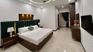Une chambre à coucher moderne avec un grand lit, une table de chevet, un téléviseur et un luminaire fixé au plafond.