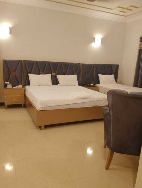 Ein Hotelzimmer mit zwei Betten, einem Nachttisch, einem Sessel und einer Deckenleuchte.
