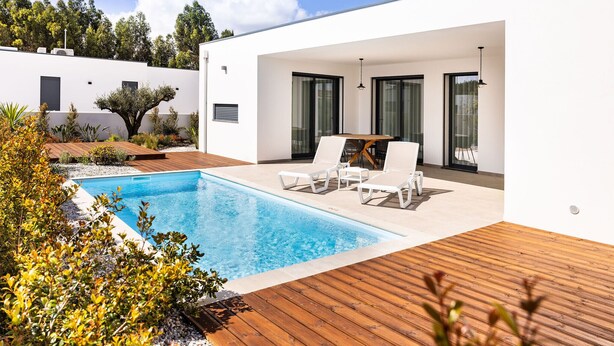 A modern outdoor pool area with a wooden deck, lounge chairs, and a dining table. - Vale Paraíso Villa - BY SCH (São Martinho do Porto)