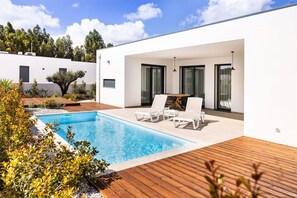 Un área de piscina moderna al aire libre con una terraza de madera, sillas de descanso y una mesa de comedor.