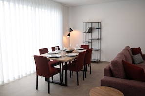 Un coin repas avec une table dressée pour quatre personnes, des chaises rouges, un lampadaire noir et une bibliothèque.