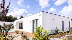 A modern white building with a pool, surrounded by a garden with various plants and a wooden deck. - Vale Paraíso Villa - BY SCH (São Martinho do Porto)