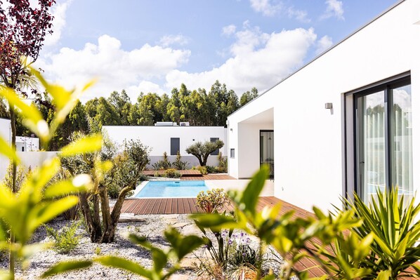 Una casa moderna con piscina, rodeada de vegetación y un cielo despejado.