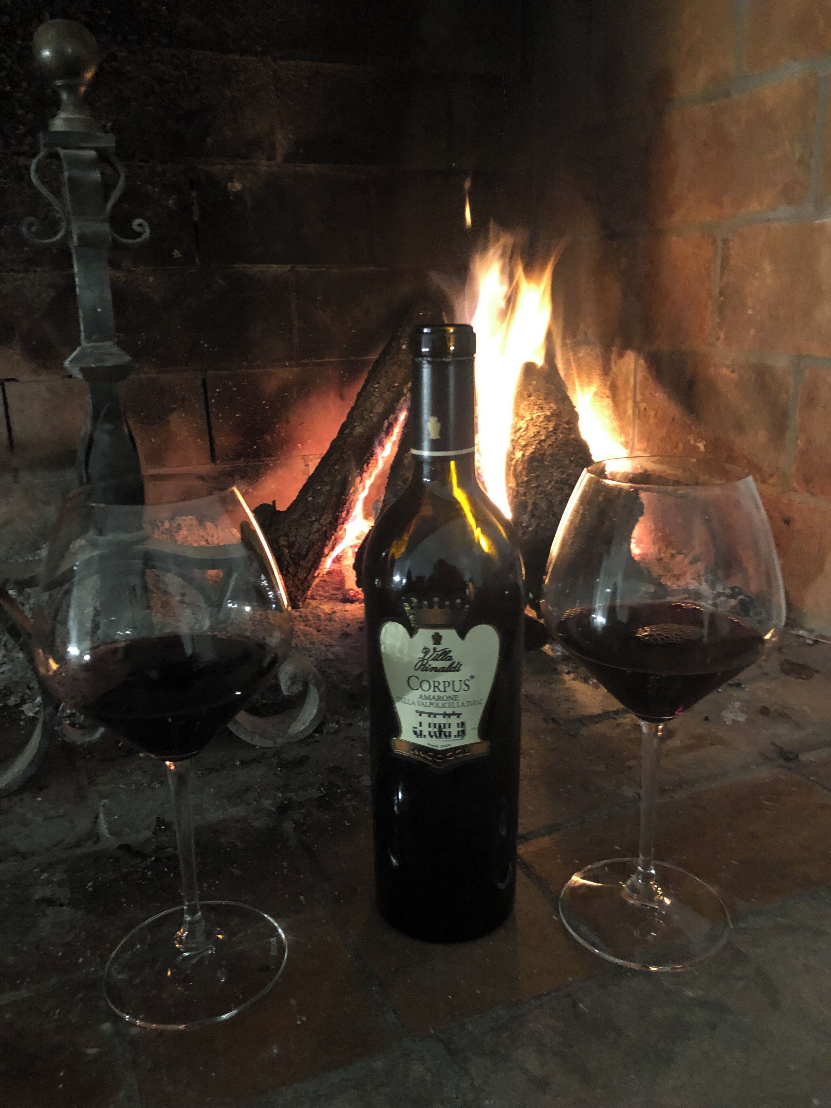 A bottle of wine and two glasses on a table in front of a fireplace.