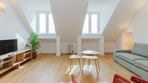 Een modern loft appartement met een hoge plafond, houten vloer, een flatscreen televisie, een groene bank en twee kleine ronde tafels.