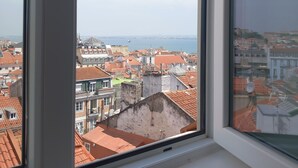 Uitzicht vanuit een raam op een stadsgezicht met rode pannendaken en een waterpartij in de verte.