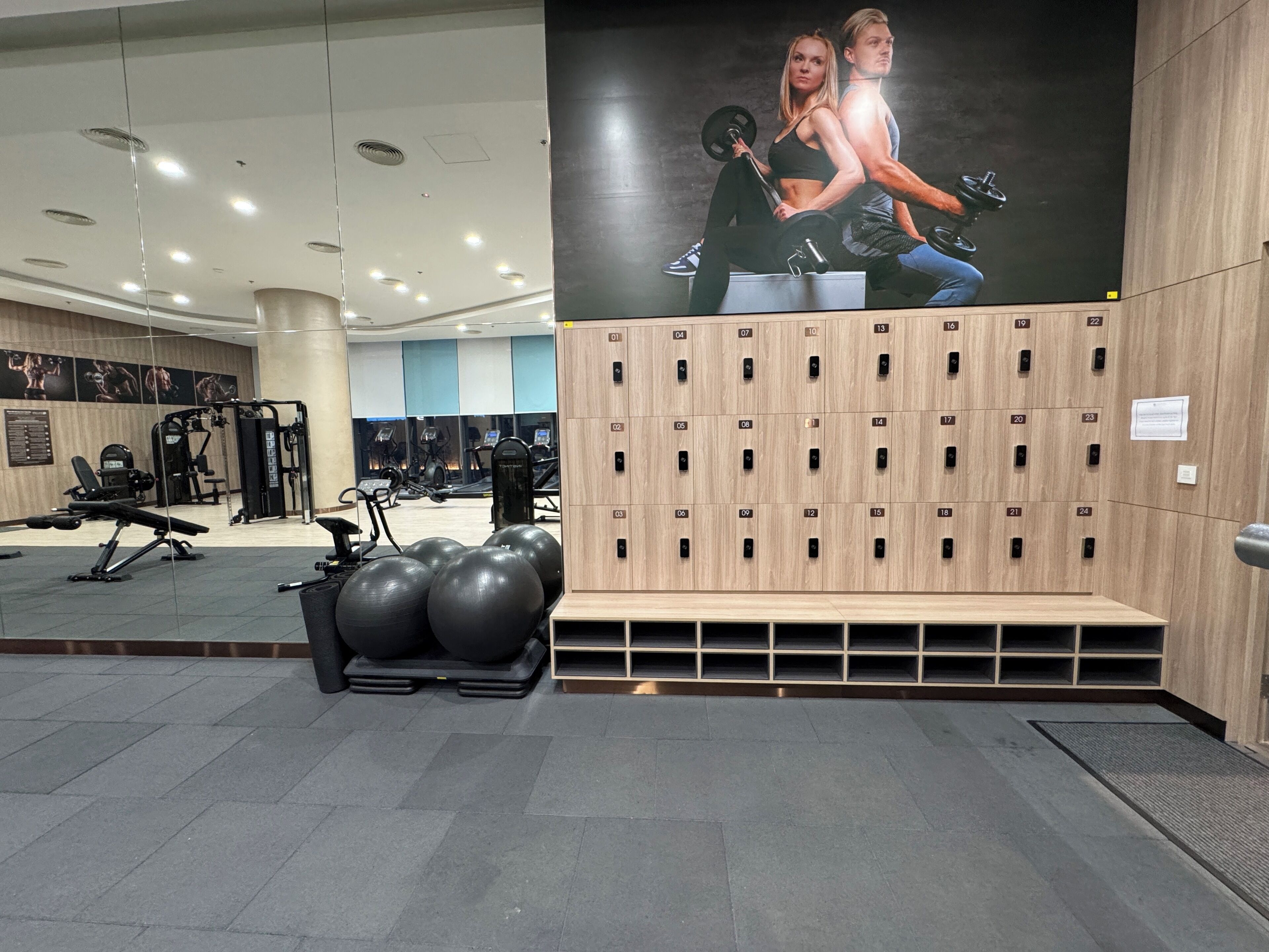 A gym with exercise equipment, a wall with lockers, and a large poster.