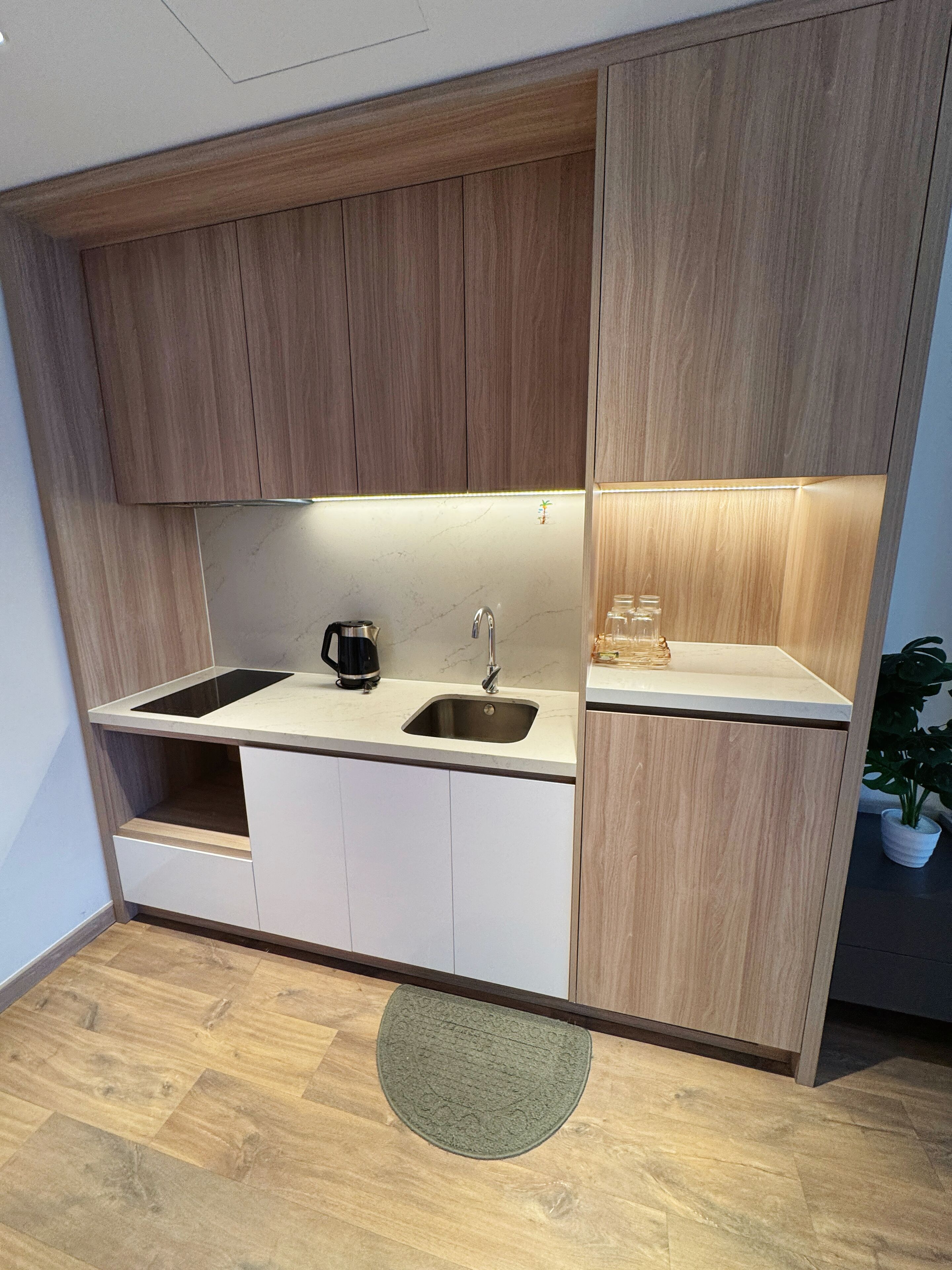 A modern kitchen with wooden cabinets, a sink, a coffee maker, and a small shelf with glassware.