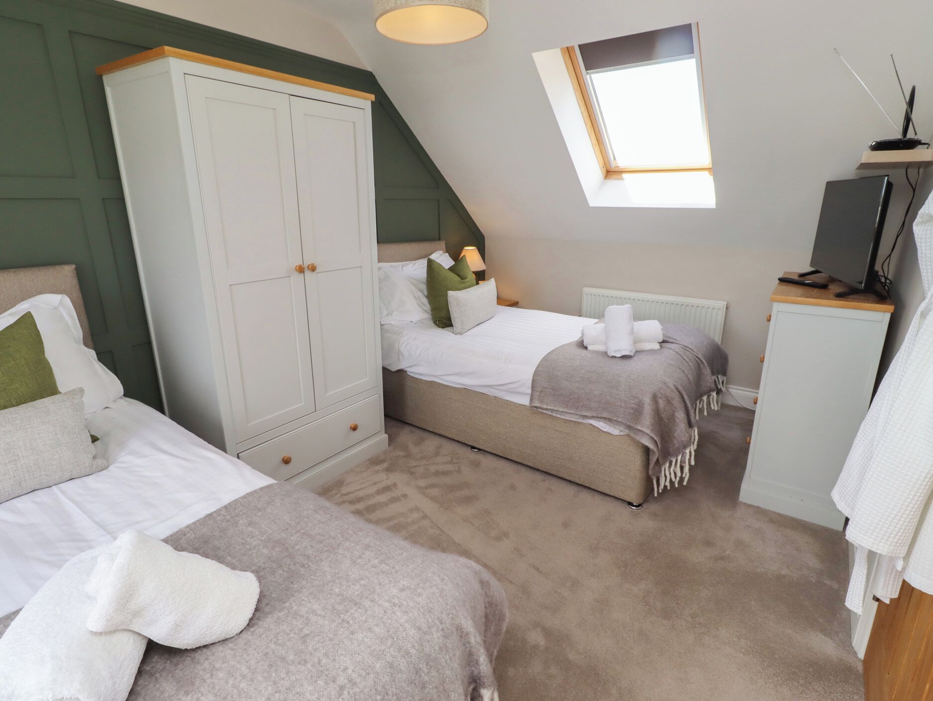 A bedroom with two beds, a wardrobe, a desk, and a skylight.