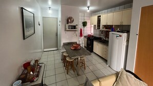 Cocina compacta con comedor, pisos de baldosas blancas y un refrigerador.