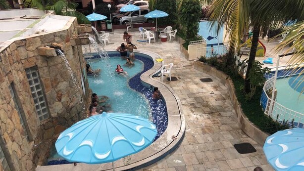 Zona de piscina con varias sombrillas, muros de piedra y área de juegos infantiles.