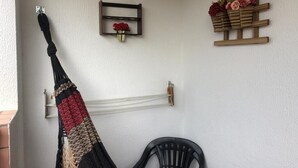 Una hamaca colgada en una pared, una silla negra, un estante con flores y un mueble de madera con flores.