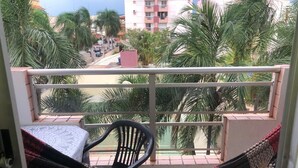 Un balcón con una hamaca, una silla y vistas a palmeras y edificios.