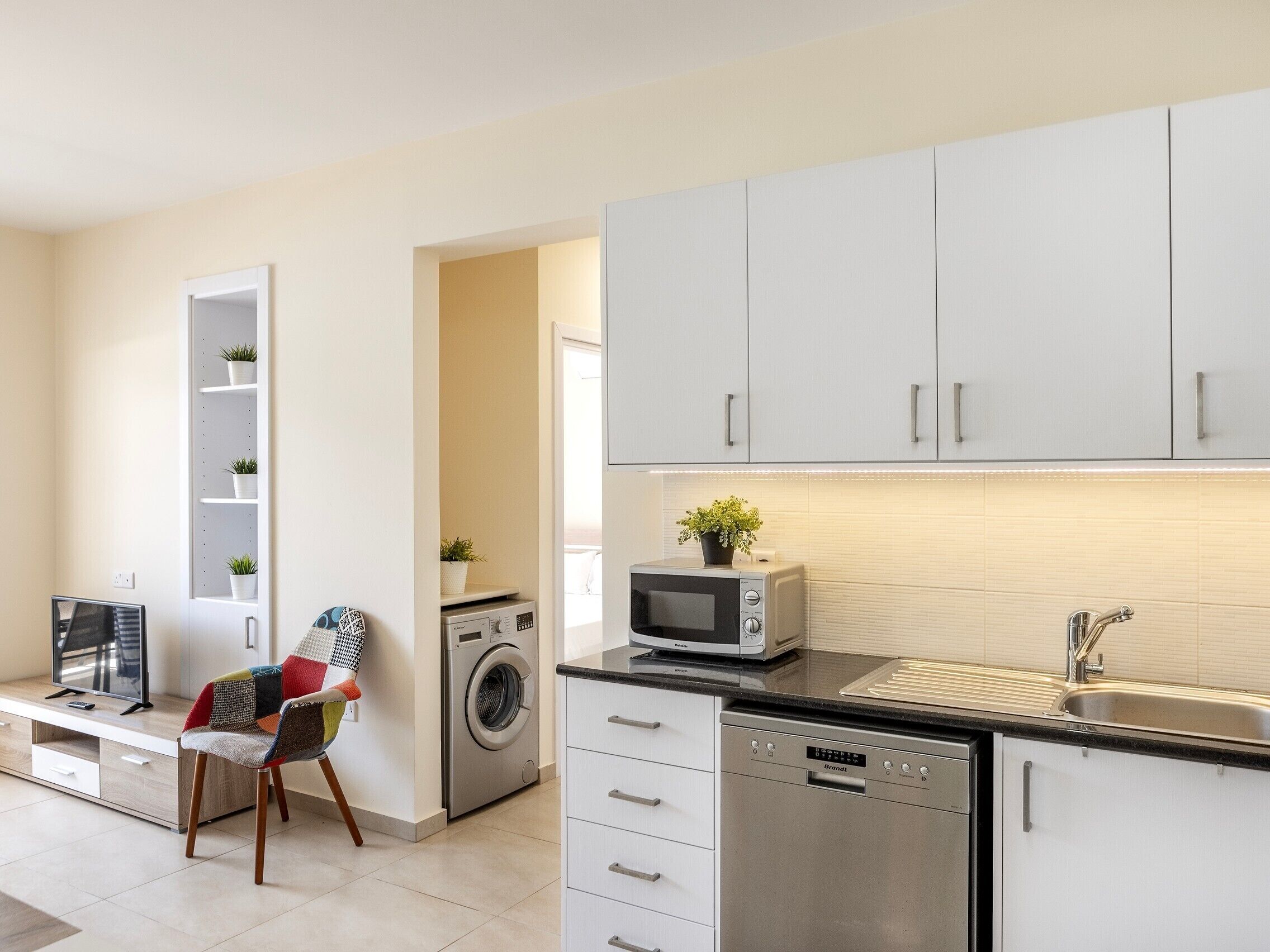 A modern kitchen with white cabinets, a built-in microwave, a dishwasher, and a washing machine.