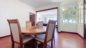 Un comedor con una mesa de madera y cuatro sillas, un espejo grande, y vistas a otra zona de comedor a través de una puerta de cristal.