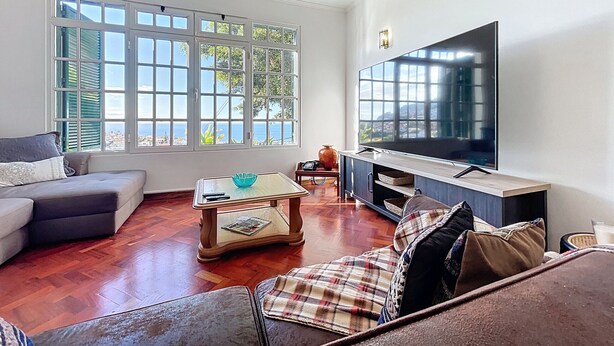 Una sala de estar con televisor grande, sofá, mesa de centro y vista al mar a través de amplios ventanales.