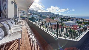 Un balcón con mobiliario exterior, vistas a un pueblo costero y cielo despejado.
