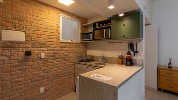 Una cocina con pared de ladrillo, microondas empotrado y un mueble verde sobre el fregadero.