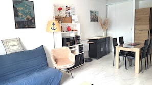 Un espace de vie compact comprenant un canapé, un fauteuil, une table à manger avec des chaises, une machine à café, un meuble et une carte accrochée au mur.