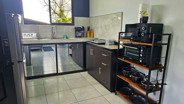 Una cocina moderna con un ventanal grande, electrodomésticos de acero inoxidable y una estantería negra con ollas.