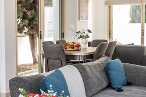 A modern living room with a gray sofa, a dining table with chairs, and a vase of flowers. - 3 bedroom villa in Pernera (pernera)
