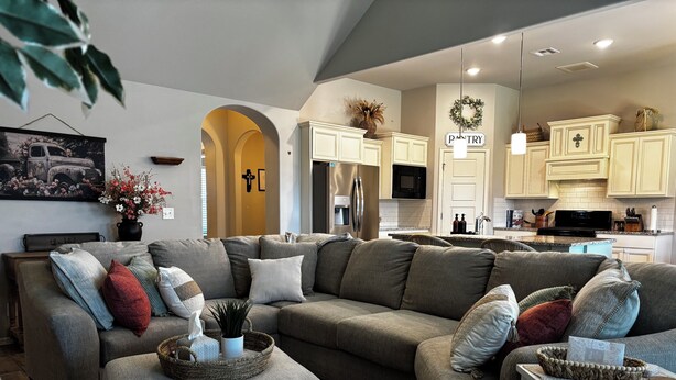 A modern living room with a sectional sofa, ottoman, and a kitchen in the background.
